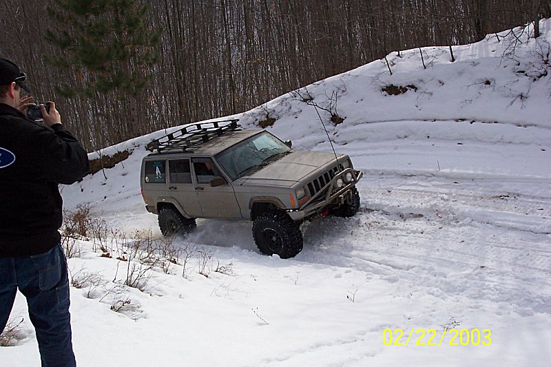 Tan Jeep Cherokee XJ with roof rack driving in snow, front bumper modified