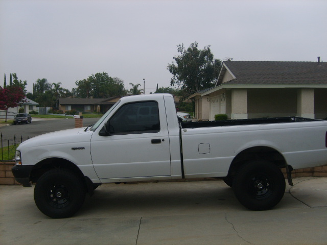 White regular-cab Ford Ranger pickup, side view, lifted with black steel wheels, parked in a driveway