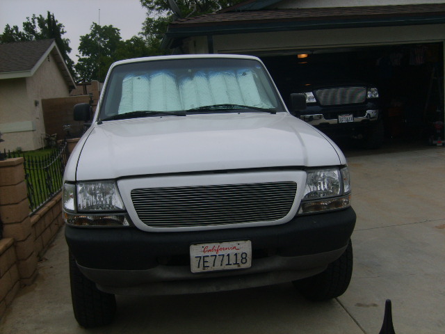 Front of white pickup with billet grille and windshield sunshade, California plate 7E77118, in driveway