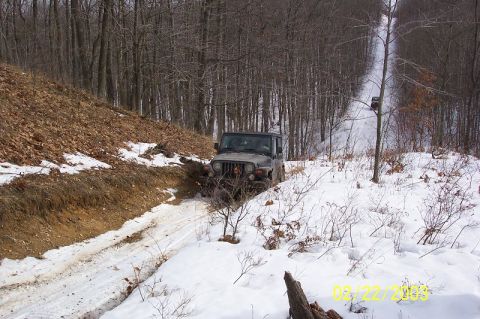 1978 Ford Bronco - A Jeep Wrangler drives through snow and mud on a wooded trail.