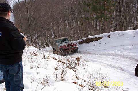 1978 Ford Bronco - A Jeep Wrangler navigates a snow-covered path through a wooded area.