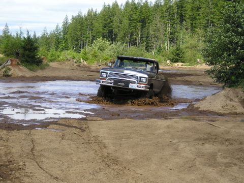 1989 Ford Bronco - Ford Bronco navigates a muddy off-road course, kicking up water and dirt.