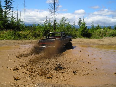 1989 Ford Bronco - A pickup truck navigates a muddy off-road course, sending mud flying.