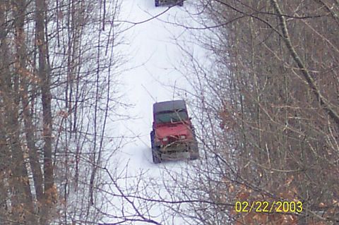 1978 Ford Bronco - Two off-road vehicles navigate a snowy path through a wooded area.