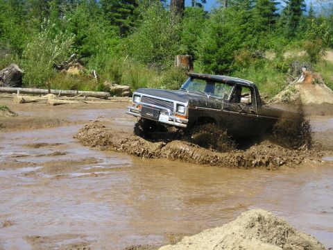 1989 Ford Bronco - A black 1979 Ford F-Series pickup truck navigates a muddy obstacle course, kicking up a large spray.