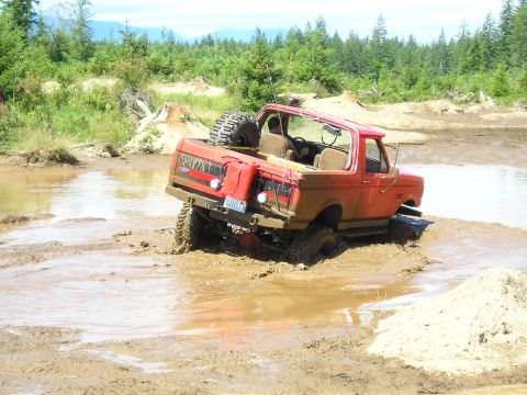1989 Ford Bronco - Off-road Bronco navigating a muddy trail with a spare tire on the back.