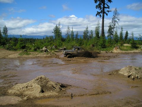 1989 Ford Bronco - A Ford F-Series truck navigates a challenging muddy terrain, sending mud flying.