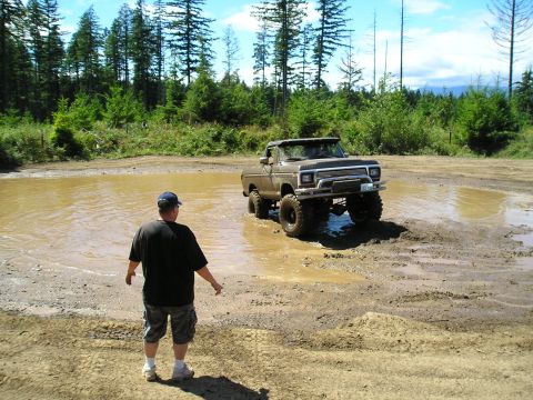 1989 Ford Bronco - Off-road pickup truck navigates a muddy terrain with a person observing the action.