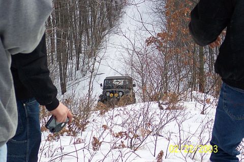 1978 Ford Bronco - A dark Jeep CJ-5 navigates a snowy path, its four yellow headlights cutting through the winter landscape.