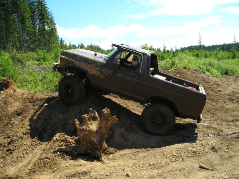 1989 Ford Bronco - A driver navigates a lifted Ford Bronco through a muddy, wooded terrain.