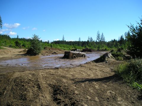 1989 Ford Bronco - Two trucks navigate a challenging muddy terrain under a clear blue sky.