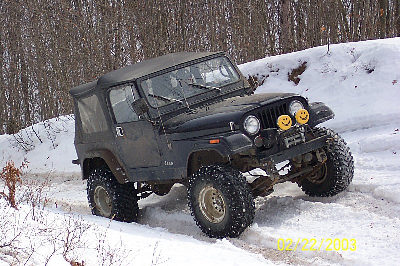 Black Jeep Wrangler with soft top driving in snow, two smiley face lights on front bumper