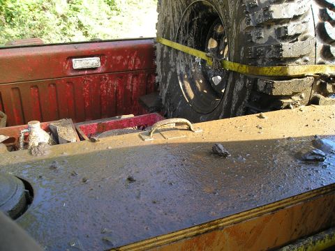 1989 Ford Bronco - Spare tire and cargo area of a muddy vehicle with some tools visible.