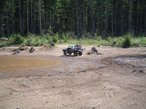 1989 Ford Bronco - A gray pickup truck navigates a muddy, off-road terrain with a forest in the background.