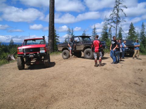 1989 Ford Bronco - Several off-road vehicles and people gathered on a dirt track under a cloudy sky.
