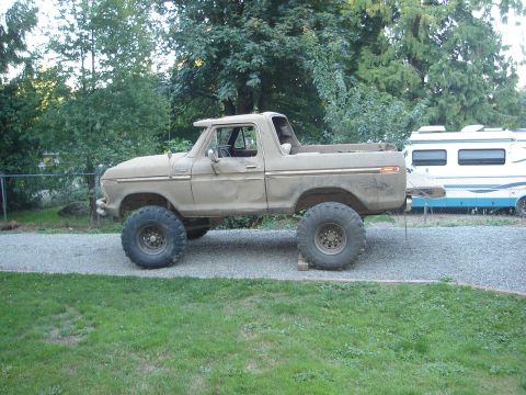 1989 Ford Bronco - This lifted 1978 Ford Bronco features oversized tires and a weathered exterior, parked next to a recreational vehicle.
