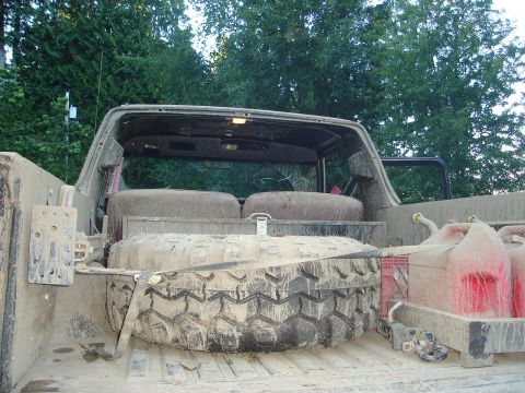 1989 Ford Bronco - The rear interior and cargo area of a mud-covered 1980s Ford Bronco, equipped with a spare tire and red gas cans.