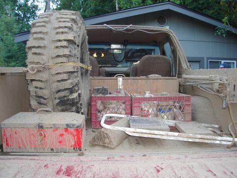 1989 Ford Bronco - The interior of a mud-covered SUV is packed with gear, including a spare tire and two milk crates.
