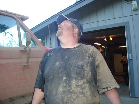 1989 Ford Bronco - A man covered in mud stands next to a red vehicle, looking up towards the sky.