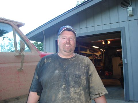 1989 Ford Bronco - A man in a muddy t-shirt and Ford cap stands beside a mud-splattered red pickup truck.