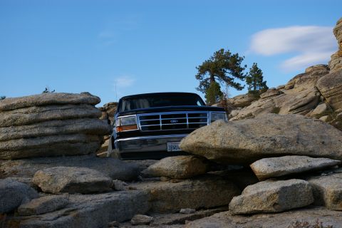 1996 Ford Bronco - 1996 Ford Bronco navigating a rocky trail under a clear blue sky.