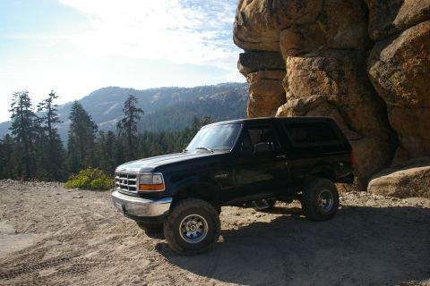 1996 Ford Bronco - This black Ford Bronco is parked on a dirt road with a mountainous forest in the background.