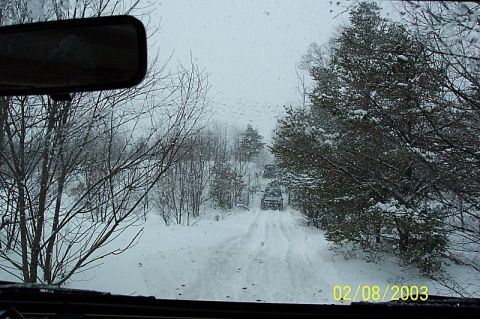 1978 Ford Bronco - Multiple SUVs navigate a snow-covered road through a wooded area.