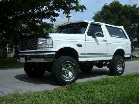 1995 Ford Bronco - This lifted SUV is parked on the side of the road with grass and trees in the background.