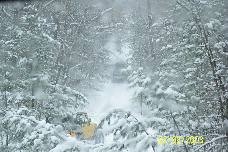 yellow vehicle driving on a snow-covered road through trees