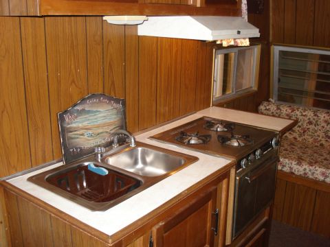 1994 Ford Bronco - The interior of a camper features a kitchen area with a sink and stove, alongside a bench seat upholstered in a floral pattern.