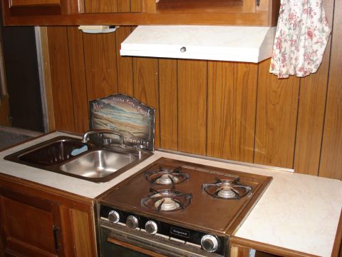 1994 Ford Bronco - Interior view of a camper kitchen a sink and stovetop, with wood-paneled walls.