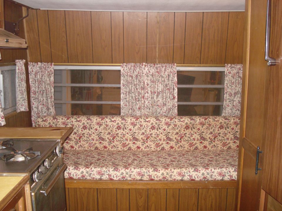 Camper interior with floral patterned couch and curtains, wood paneling, and a stove