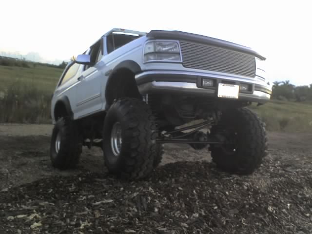 Lifted white Ford Bronco with large tires, front end angled up on a dirt mound