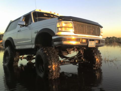 1995 Ford Bronco - Lifted 1995 Ford Bronco driving through shallow water at sunset.