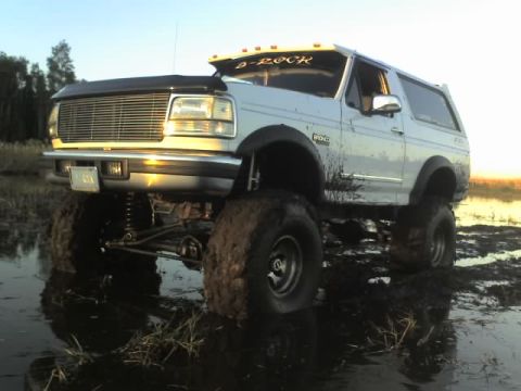 1995 Ford Bronco - Modified 1995 Ford Bronco deep in mud, showing off its lifted suspension and large off-road tires.