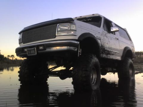 1995 Ford Bronco - This lifted Ford Bronco is shown in shallow water with mud splattered on its body.