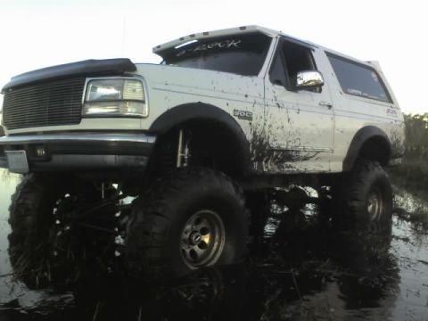 1995 Ford Bronco - Mud-covered 1995 Ford Bronco with oversized tires navigating a muddy terrain.