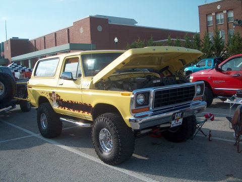 1978 Ford Bronco - Yellow 1978 Ford Bronco on display, hood open, with other trucks nearby.