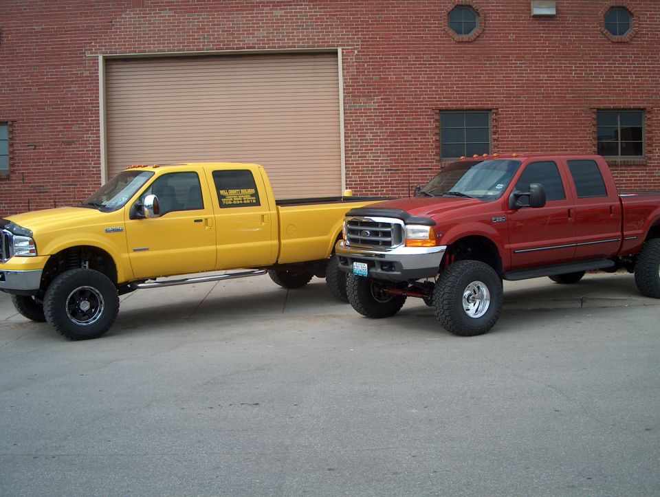 Yellow and red lifted pickup trucks parked outside a brick building with a large garage door