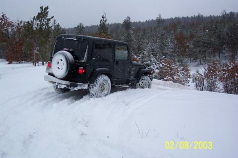 1978 Ford Bronco - A black Jeep Wrangler navigates a snowy, wooded landscape.