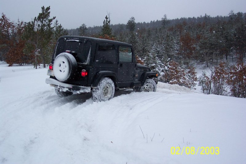 Black Jeep Wrangler driving in deep snow on a wooded trail