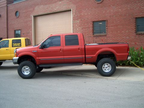1978 Ford Bronco - A red Ford F-350 pickup truck is parked next to a yellow truck in front of a brick building.