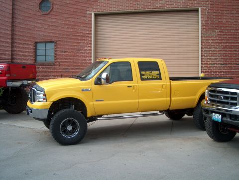 1978 Ford Bronco - A yellow Ford F-250 Super Duty pickup truck is parked next to another truck, with text visible on its door.