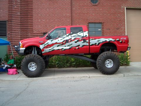 1978 Ford Bronco - A heavily modified red pickup truck with oversized tires and custom graphics is parked on a street.