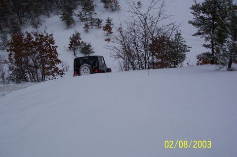 1978 Ford Bronco - A Jeep navigates through a snowy landscape with trees on a hill.