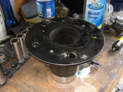 1994 Ford Bronco - A close-up view of a black metal automotive part with multiple bolt holes, resting on a workbench with various tools and cleaning supplies.