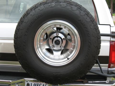 1994 Ford Bronco - Close-up of a Nitto Terra Grappler all-terrain spare tire on a polished five-spoke American Racing-style alloy wheel with exposed rivets, m…