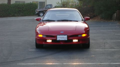 1996 Ford Probe - Front view of a red 1996 Ford Probe parked in a lot. A brown pickup truck is visible in the background.