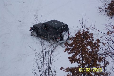 1978 Ford Bronco - A black SUV is partially submerged in snow, with bare trees and falling snow visible.