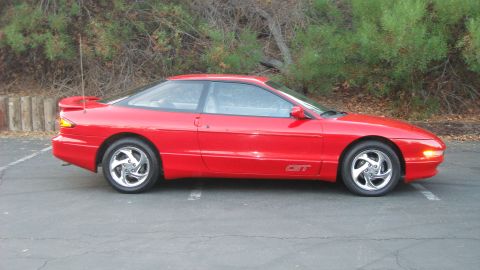 1996 Ford Probe - A red 1996 Ford Probe GT is shown from the side, parked outdoors with trees in the background.